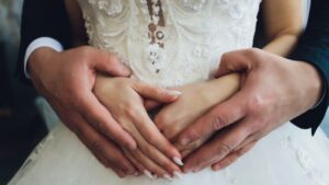 Older man hands grasping young girl hands over white wedding dress
